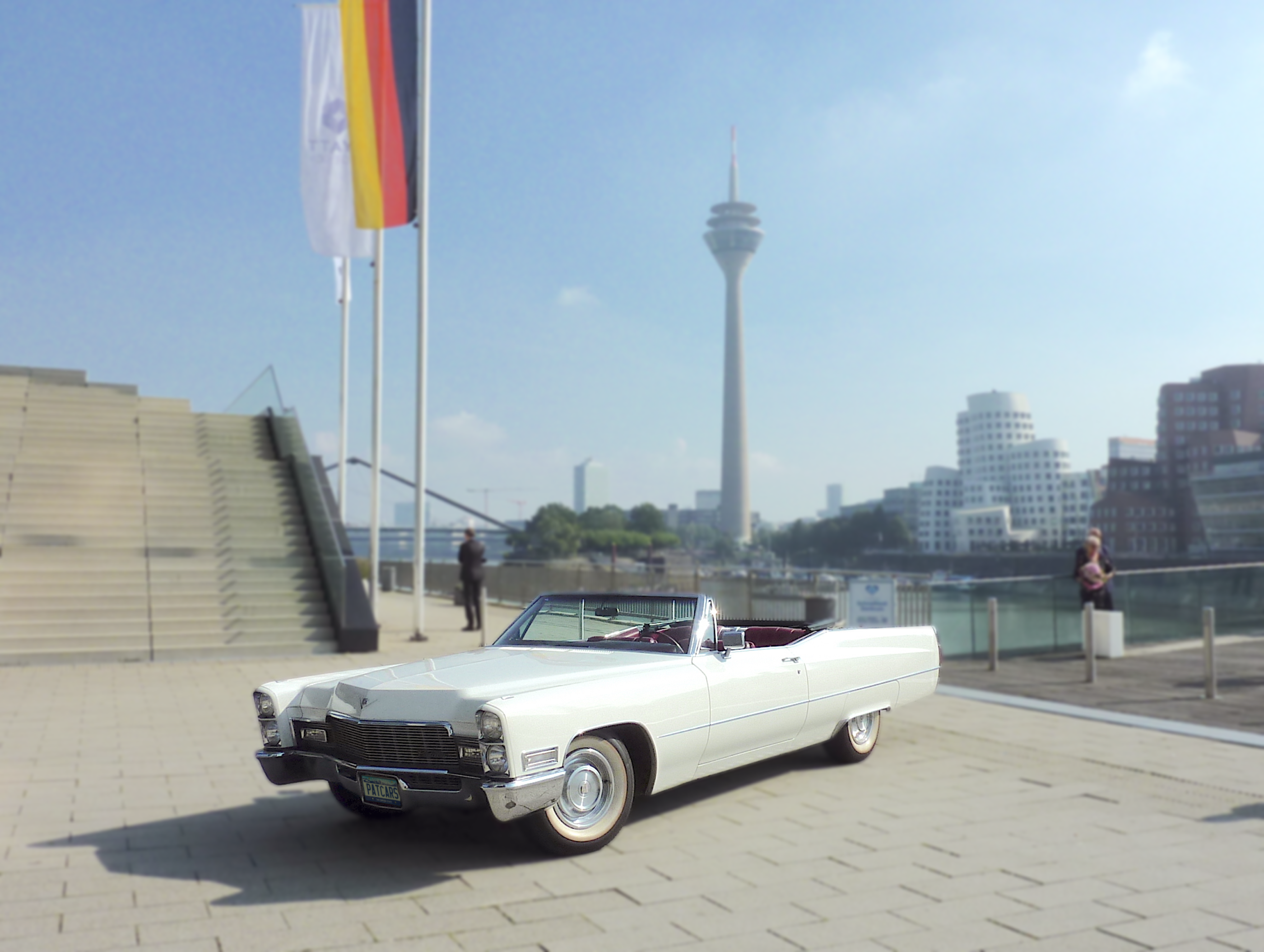 Unser Cadillac Convertible Baujahr 1968 steht prominent vor dem Hyatt Hotel im Medienhafen Düsseldorf mit dem Fernsehturm im Hintergrund.